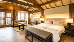 A spacious hotel room with a large bed, a sofa, a bench, and a dining table. - Lijang First Bay Hotel (Lijiang)