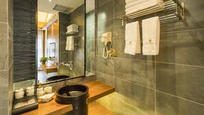A modern bathroom with a large mirror, dark tiled walls, a wooden vanity, a black basin, and neatly arranged white towels. - Lijang First Bay Hotel (Lijiang)