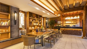 A restaurant with a long wooden table, wicker chairs, and shelves with books and decorative items. - Lijang First Bay Hotel (Lijiang)