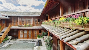 A traditional wooden building with a tiled roof, a courtyard, and a balcony with flowers. - Lijang First Bay Hotel (Lijiang)
