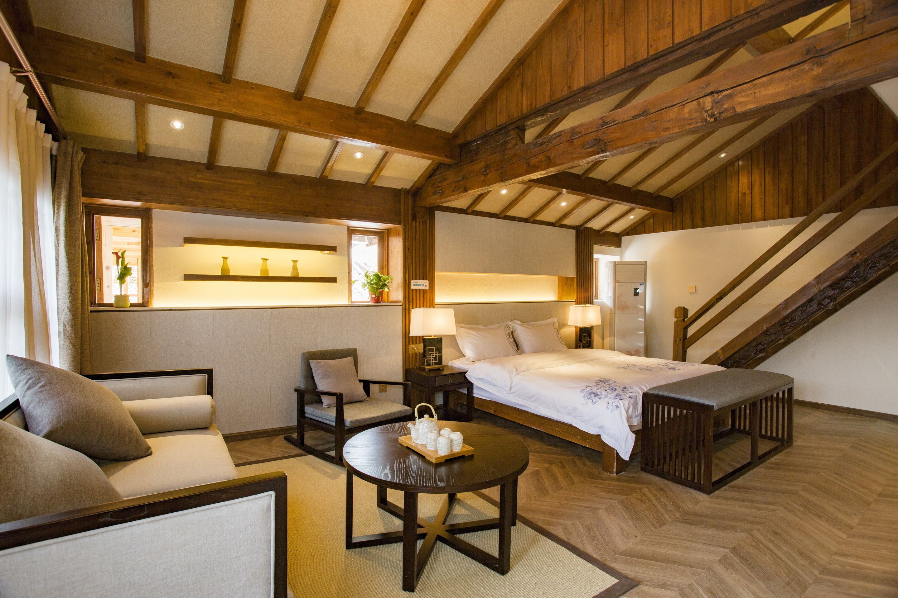 Ett mysigt hotellrum med ett träpanelat tak, en säng, en soffa, ett runt bord med diverse föremål på och en trappa.