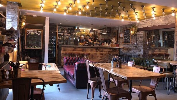 A cozy restaurant with wooden tables and chairs, a bar area, and a stone wall. - Sgwd Gwladys (Neath)