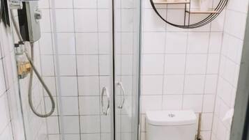 Un baño con ducha de vidrio, inodoro y estante en la pared con plantas.