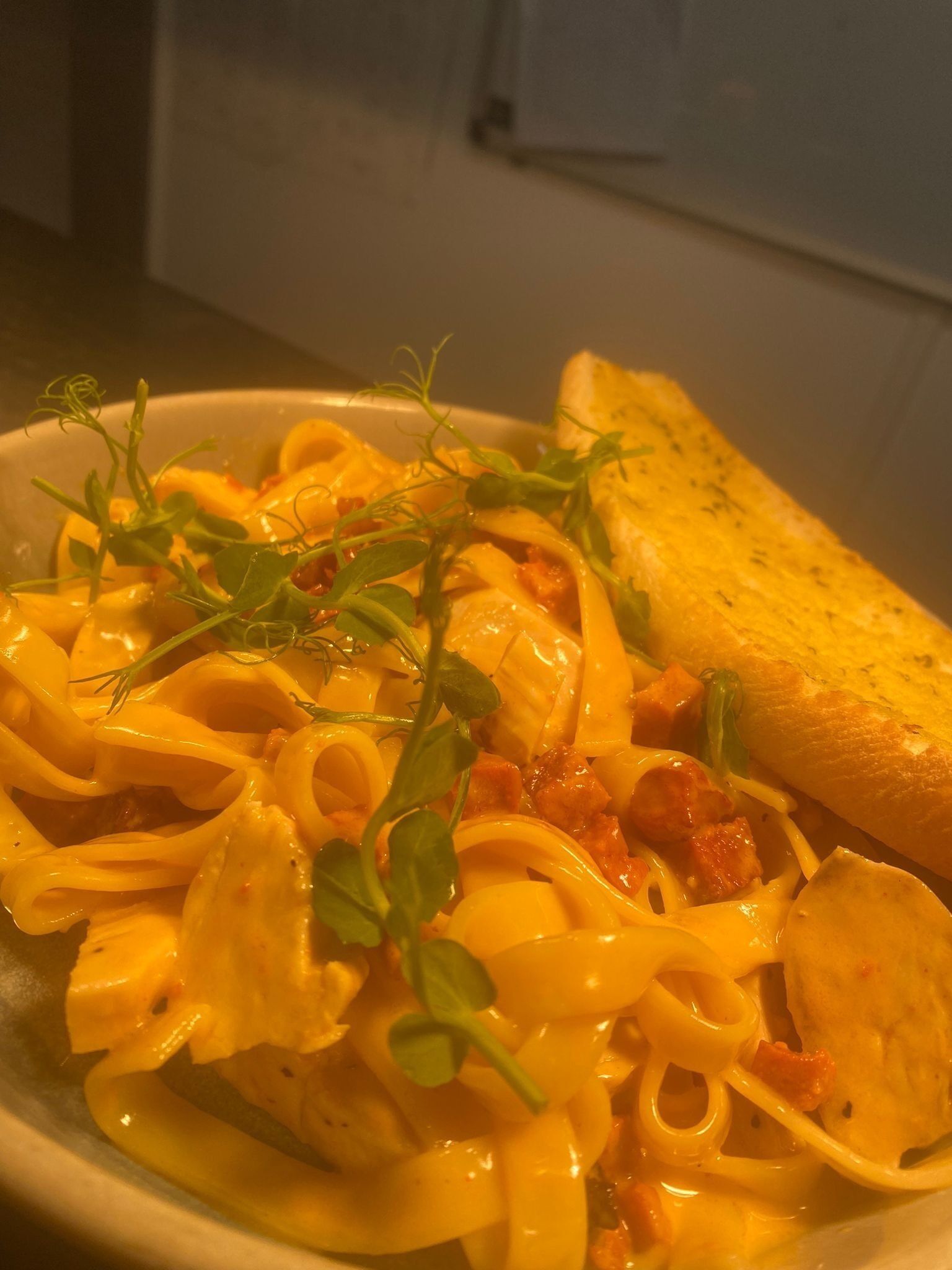 Un plato de pasta con salsa cremosa, adornado con vegetales verdes y una rebanada de pan tostado.