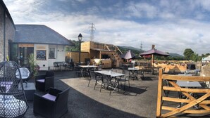 An outdoor seating area with tables and chairs, a wooden structure, and a stone wall. - Sgwd Gwladys (Neath)