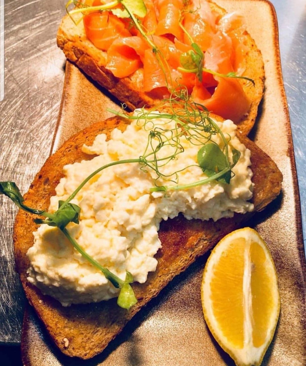 Two open-faced sandwiches on a wooden board, one with cream cheese and greens, the other with smoked salmon and greens.