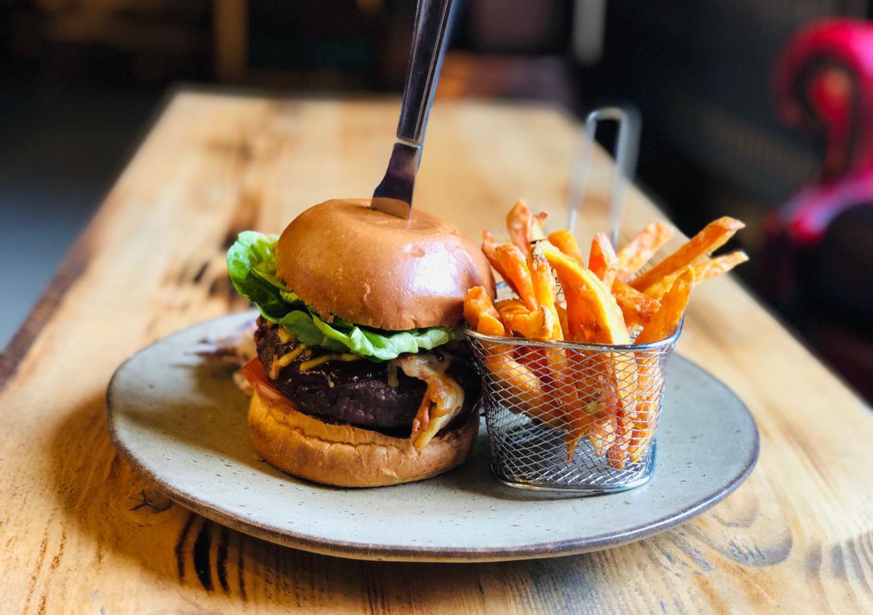 A burger with fries on a plate on a wooden table.