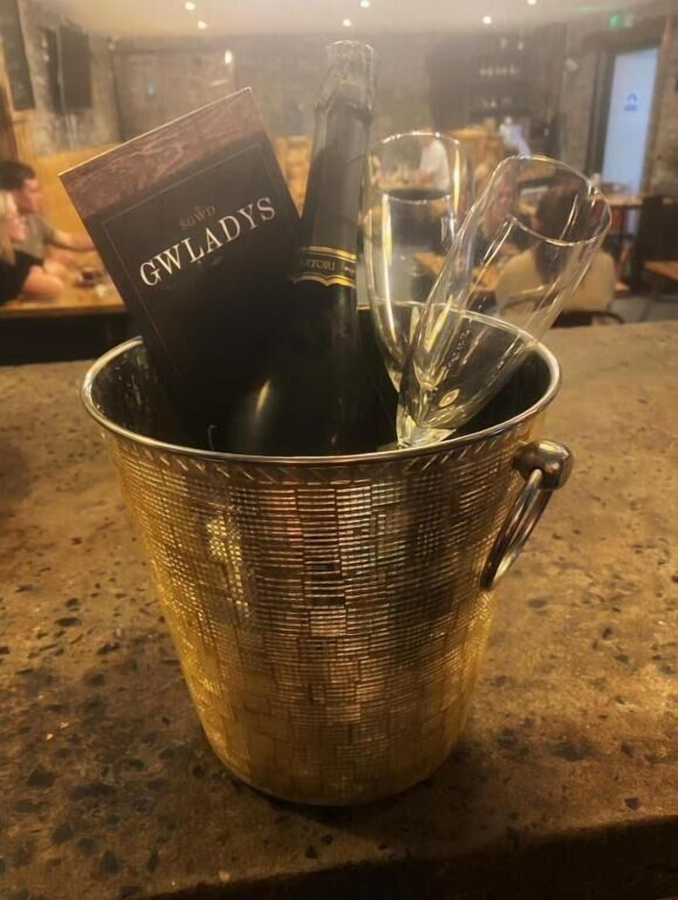 Un balde de color dorado que contiene una botella de vino y una copa.