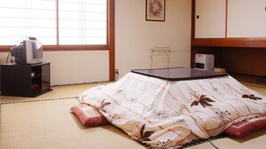 A traditional Japanese room with tatami flooring, a futon bed, a television on a low table, and a small cabinet. - Zao Onsen Pension Bokunouchi (Kaminoyama)