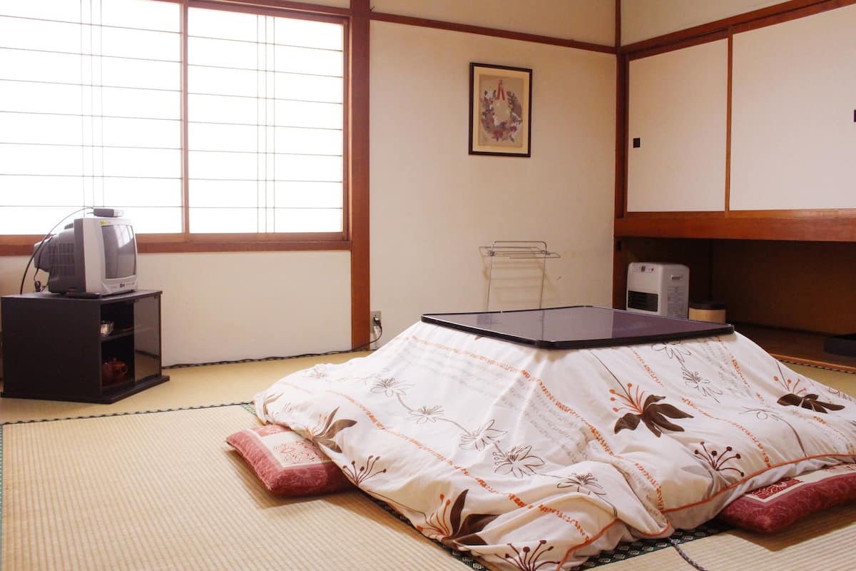 Une pièce de style japonais traditionnel, avec un sol recouvert de tatamis, un futon servant de lit, un téléviseur posé sur une petite table basse et un petit meuble.