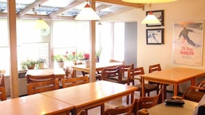 A dining area with wooden tables and chairs, potted plants, and a poster on the wall. - Zao Onsen Pension Bokunouchi (Kaminoyama)