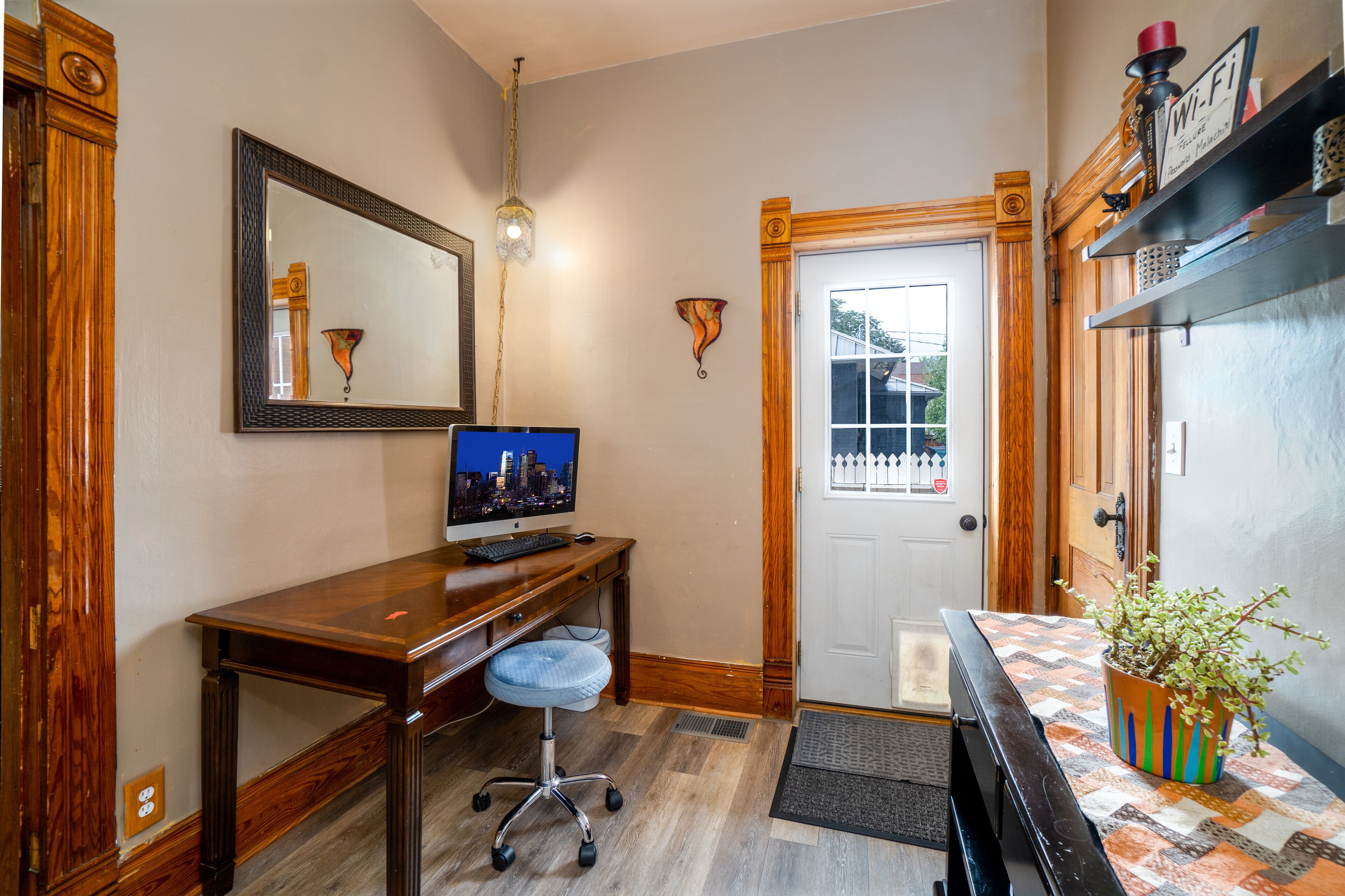 A room with a wooden desk, a computer, a chair, a door, and a potted plant.
