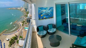 Ein Balkon mit Blick auf Strand und Meer, zwei Korbstühle mit Kissen und eine Glastür zu einem Balkon mit Geländer.
