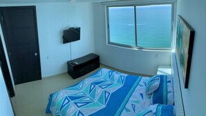 Ein Schlafzimmer mit Bett, einem an der Wand befestigten Fernseher, einem Fenster mit Meerblick und einer Tür.