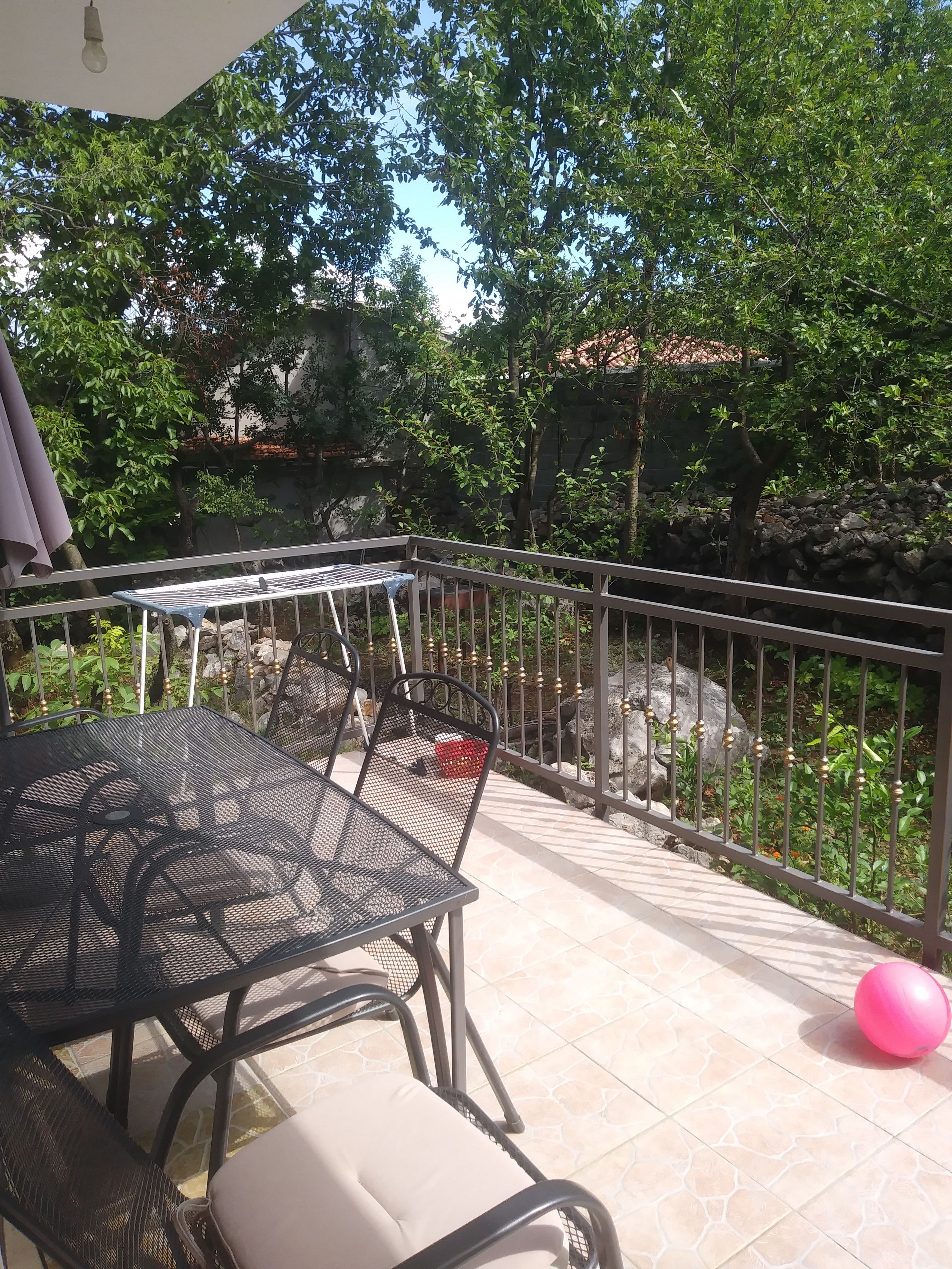 An outdoor patio with a metal table and chairs, surrounded by a stone wall and greenery.