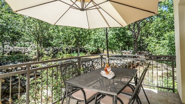 Una terrazza esterna con tavolo e sedie, un ombrellone e vista su un'area giardino rocciosa.