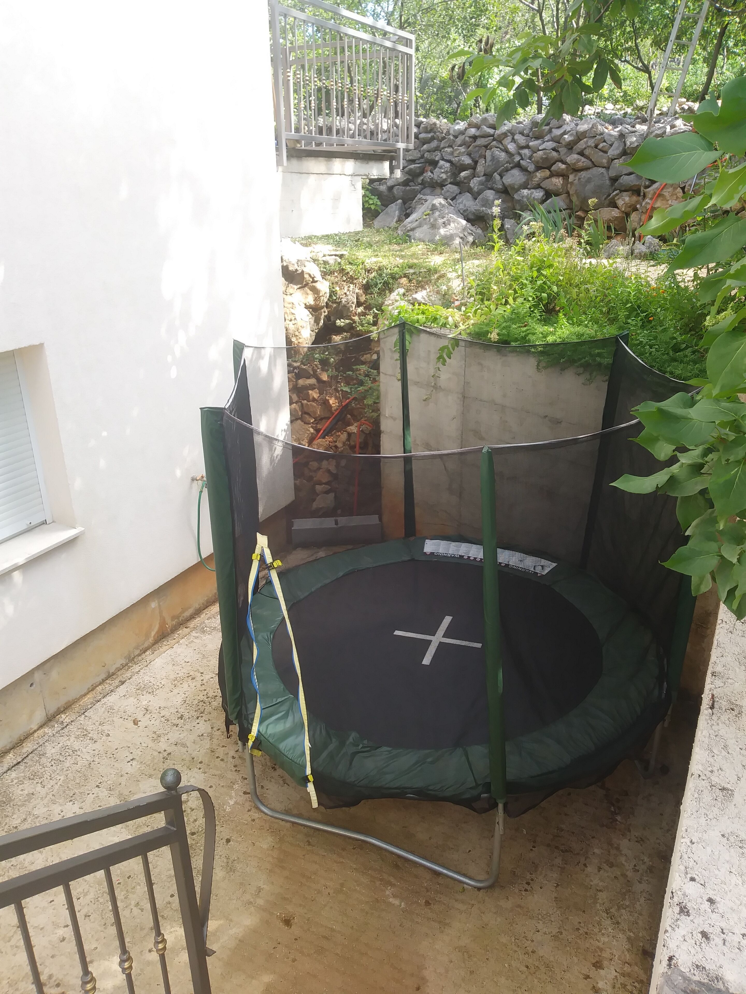 Zona pequeña de trampolines al aire libre con una pared de piedra y follaje de fondo.