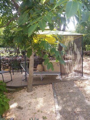 Un área de estar al aire libre cubierta con un toldo amarillo, rodeada de árboles y un camino de grava.