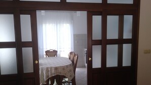 Zona pranzo con tavolo e sedie, una porta in legno con pannelli di vetro satinato e un lampadario al soffitto.