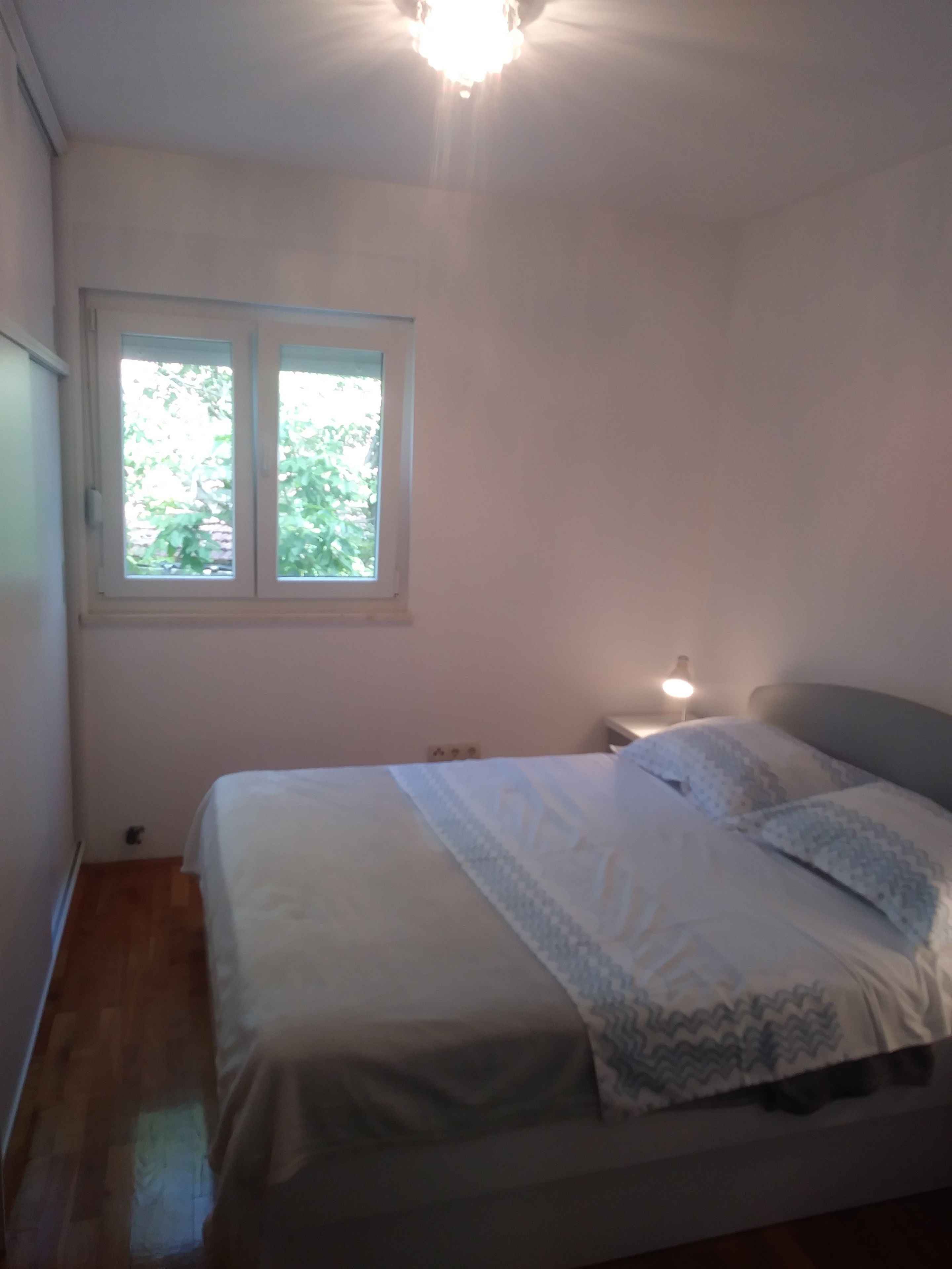 A bedroom with a bed, a window, and a nightstand with a lamp.