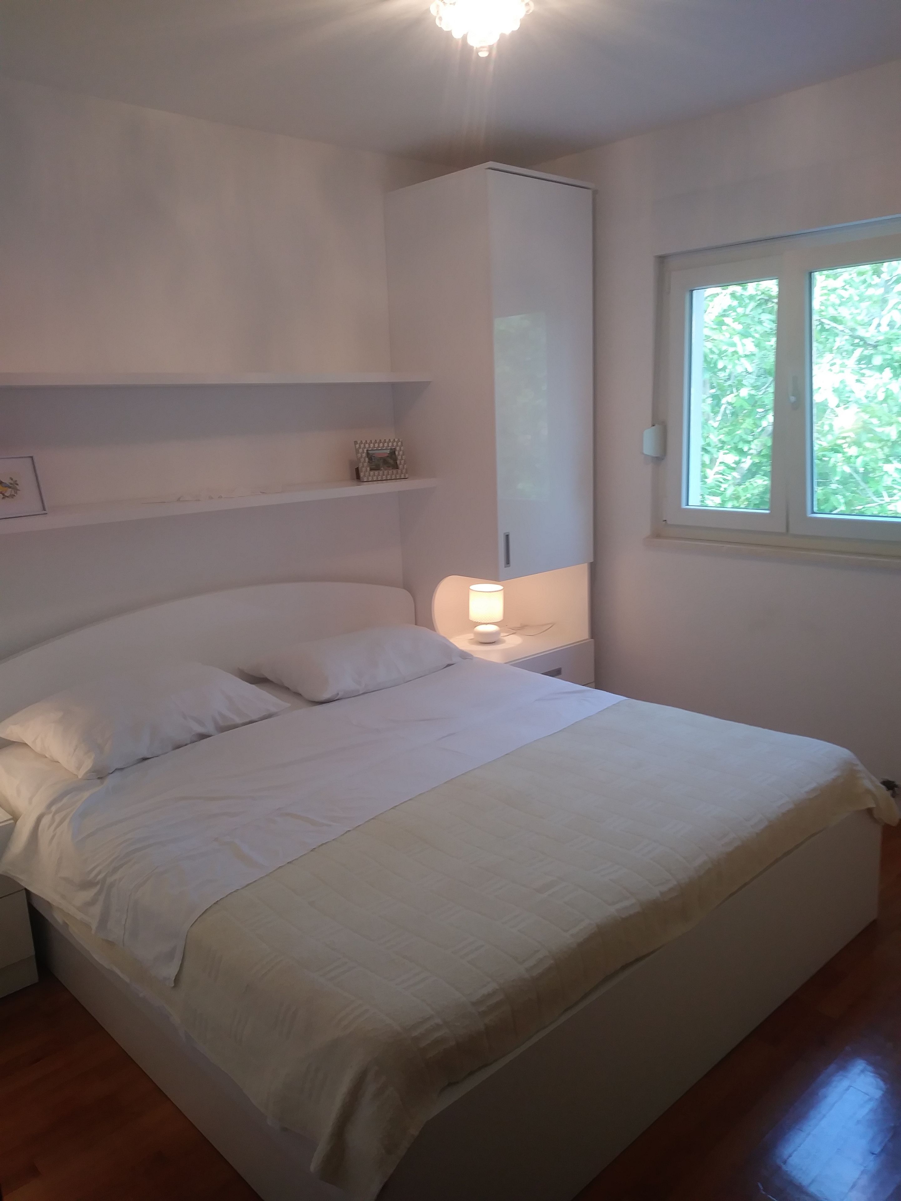 Een slaapkamer met een bed, nachtkastjes, een wandkast en een raam met uitzicht op bomen.