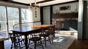 A dining area with a wooden table and chairs, a chandelier, and a view of the outdoors. - Charming 5BR Retreat on 1 Acre , Quiet Cul-de-Sac + Garden & Deck (West Barnstable)