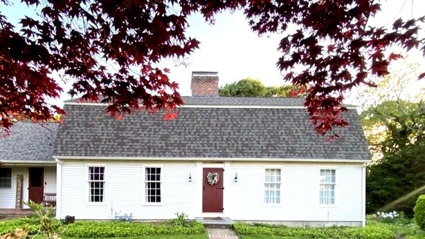 A white building with a brick roof, a front porch, and a small garden area. - Charming 5BR Retreat on 1 Acre , Quiet Cul-de-Sac + Garden & Deck (West Barnstable)