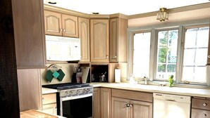 A kitchen with wooden cabinets, a stove, a dishwasher, and a trash can. - Charming 5BR Retreat on 1 Acre , Quiet Cul-de-Sac + Garden & Deck (West Barnstable)