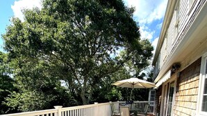 An outdoor deck with wicker furniture and a table with an umbrella. - Charming 5BR Retreat on 1 Acre , Quiet Cul-de-Sac + Garden & Deck (West Barnstable)