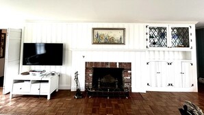 A living room with a fireplace, a television, and a cabinet with a decorative screen. - Charming 5BR Retreat on 1 Acre , Quiet Cul-de-Sac + Garden & Deck (West Barnstable)