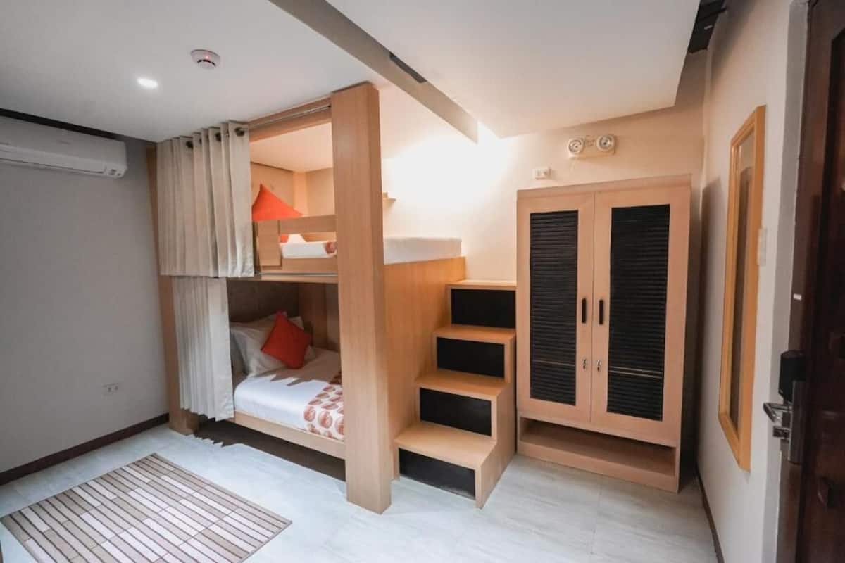 A compact room with a bunk bed, a wardrobe with sliding doors, and a small desk area.