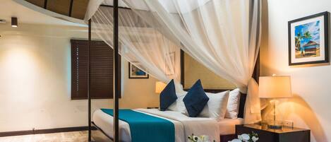 A bedroom with a four-poster bed, a nightstand with a lamp, a framed picture on the wall, and a window with blinds.