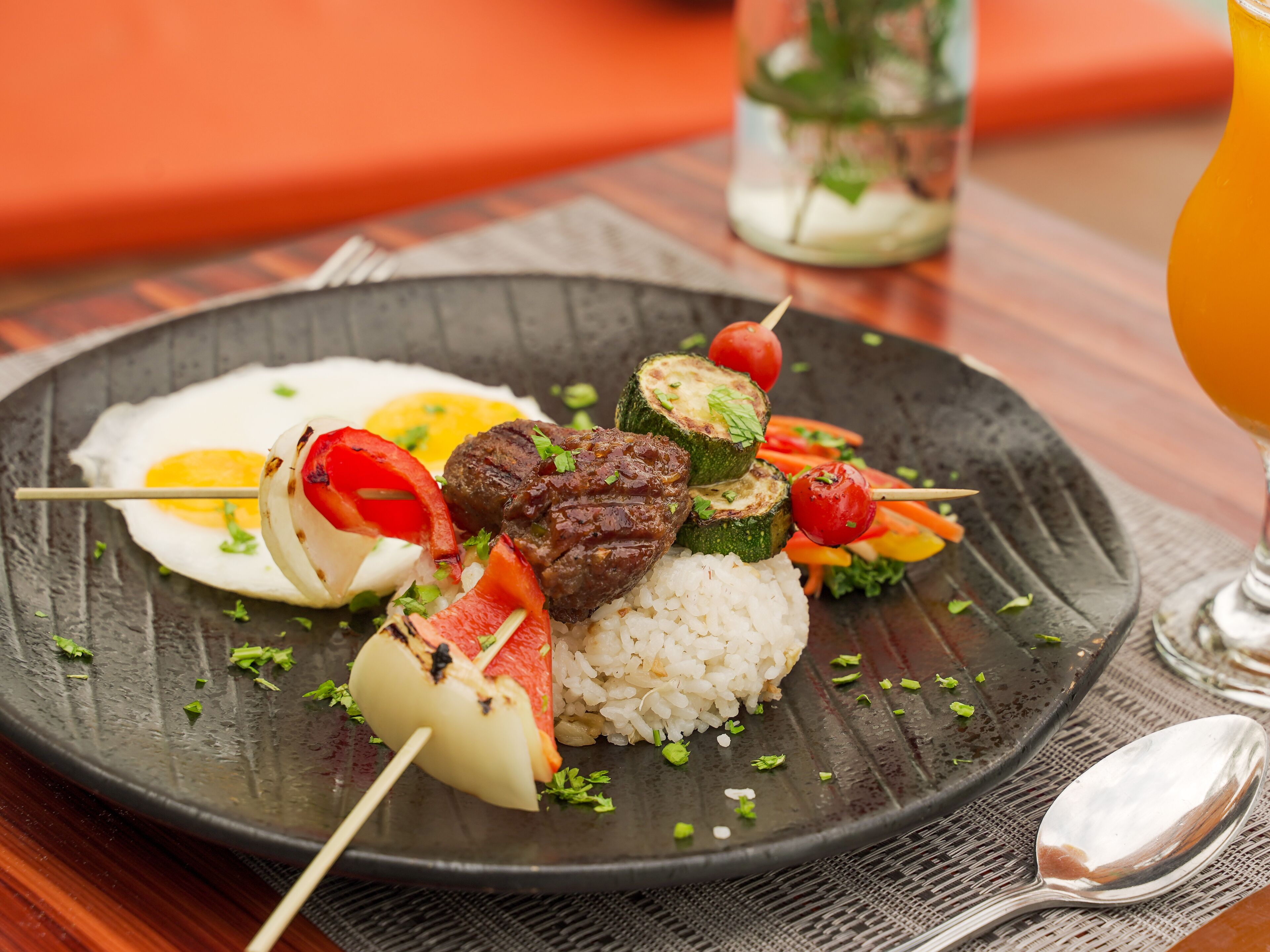 Un plato de comida con brochetas, arroz y un huevo frito.