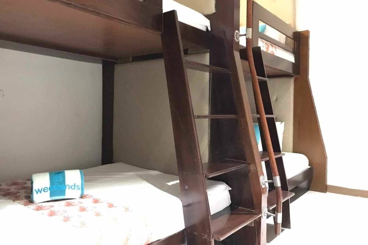 A bunk bed with a ladder, a bed with a floral bedspread, and a wall with a window.