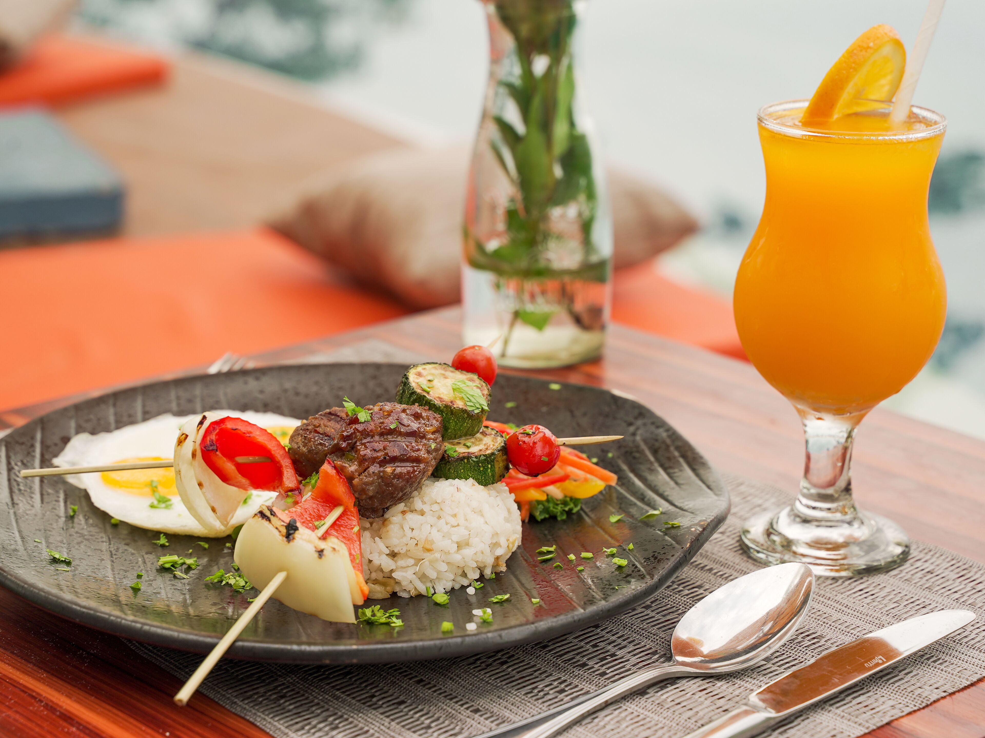 A plate of food with rice, vegetables, and meat, and a glass of orange juice on a table.