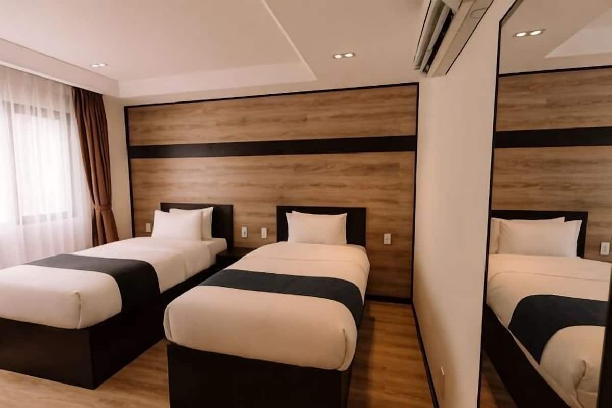 Une chambre d’hôtel avec deux lits, une tête de lit en bois, un grand miroir et une fenêtre avec des rideaux.