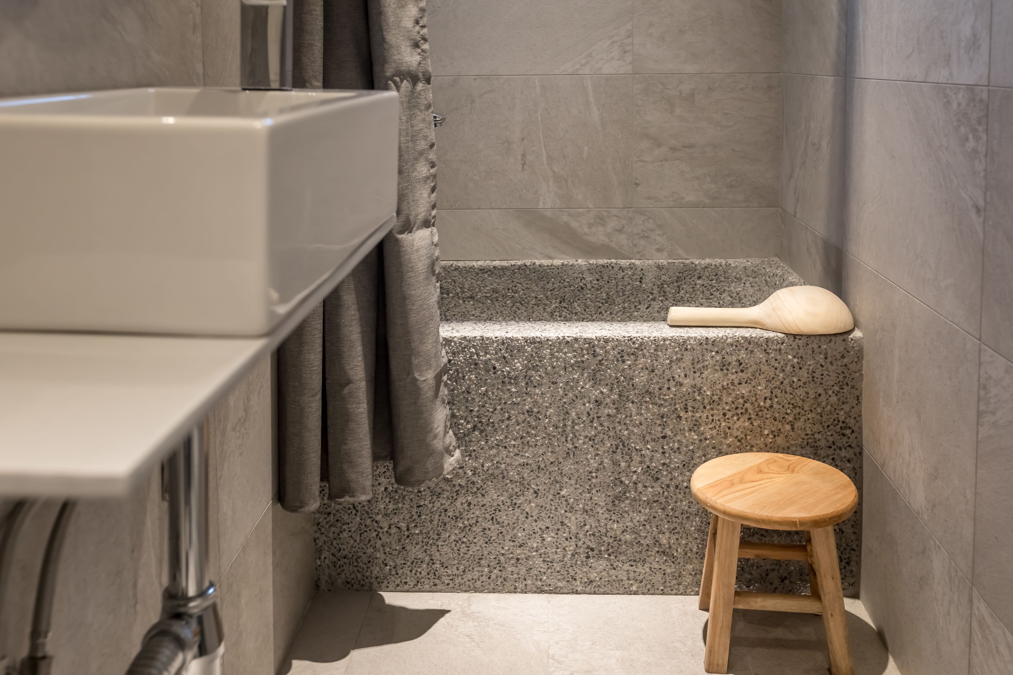 A bathroom with a bathtub, a wooden stool, and a shower curtain.
