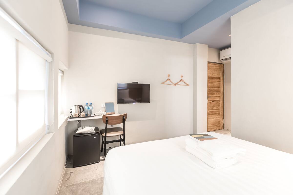A hotel room with a bed, a desk with a chair, a television, and a wardrobe.