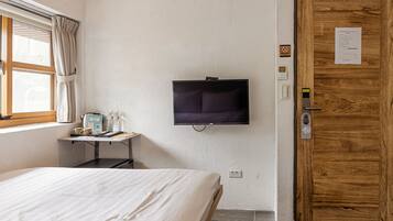 A hotel room with a bed, a television mounted on the wall, a wooden door, and a window with curtains.