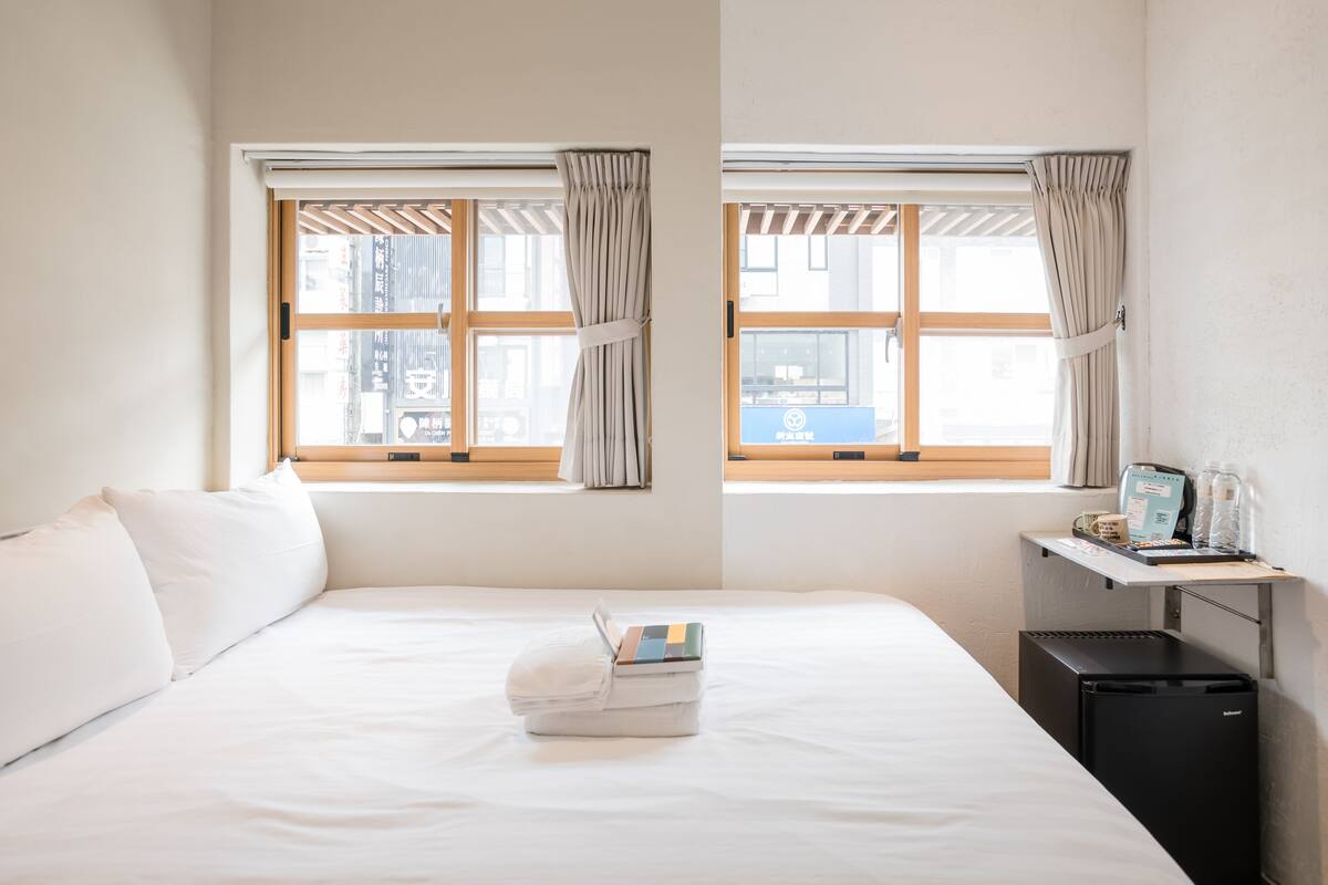 A hotel room with a bed, a desk with a computer, and a window with curtains.