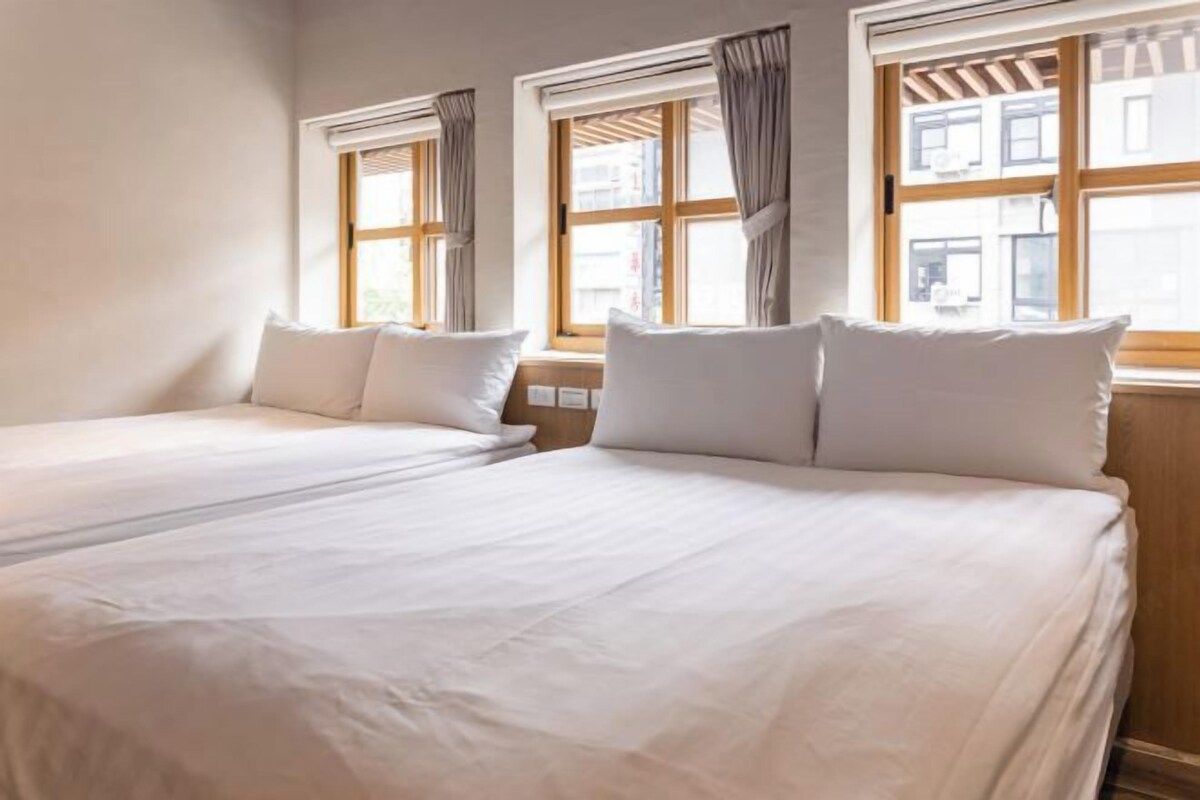 Ett hotellrum med två sängar, stora fönster med gardiner och utsikt över staden.