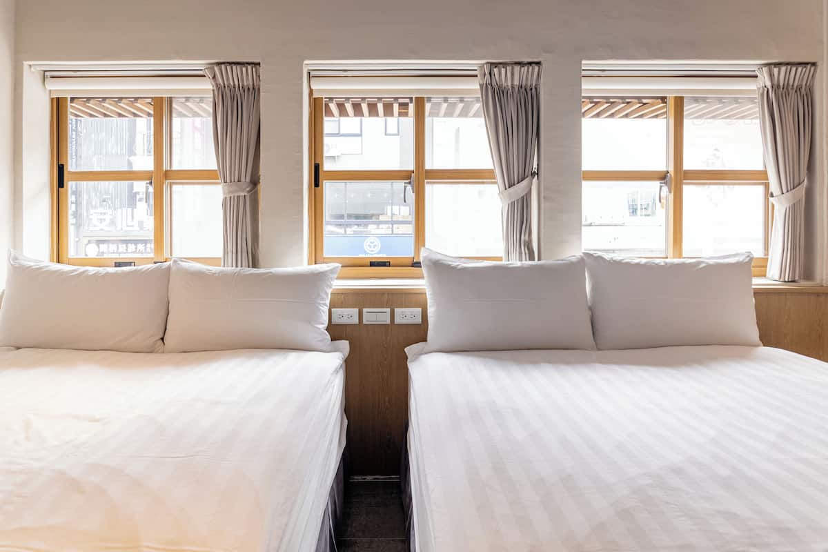 A hotel room with two beds, a window with curtains, and a view of the city.