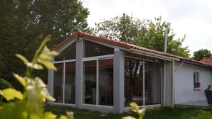 A modern house with large glass windows, a tiled roof, and a small garden area.