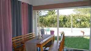 A room with a wooden bench, a table, and a view of a garden through a sliding glass door.