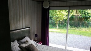 A bedroom with a bed, a lamp, and a view of the outdoors.