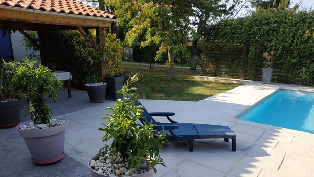 A poolside area with lounge chairs, potted plants, and a pergola.
