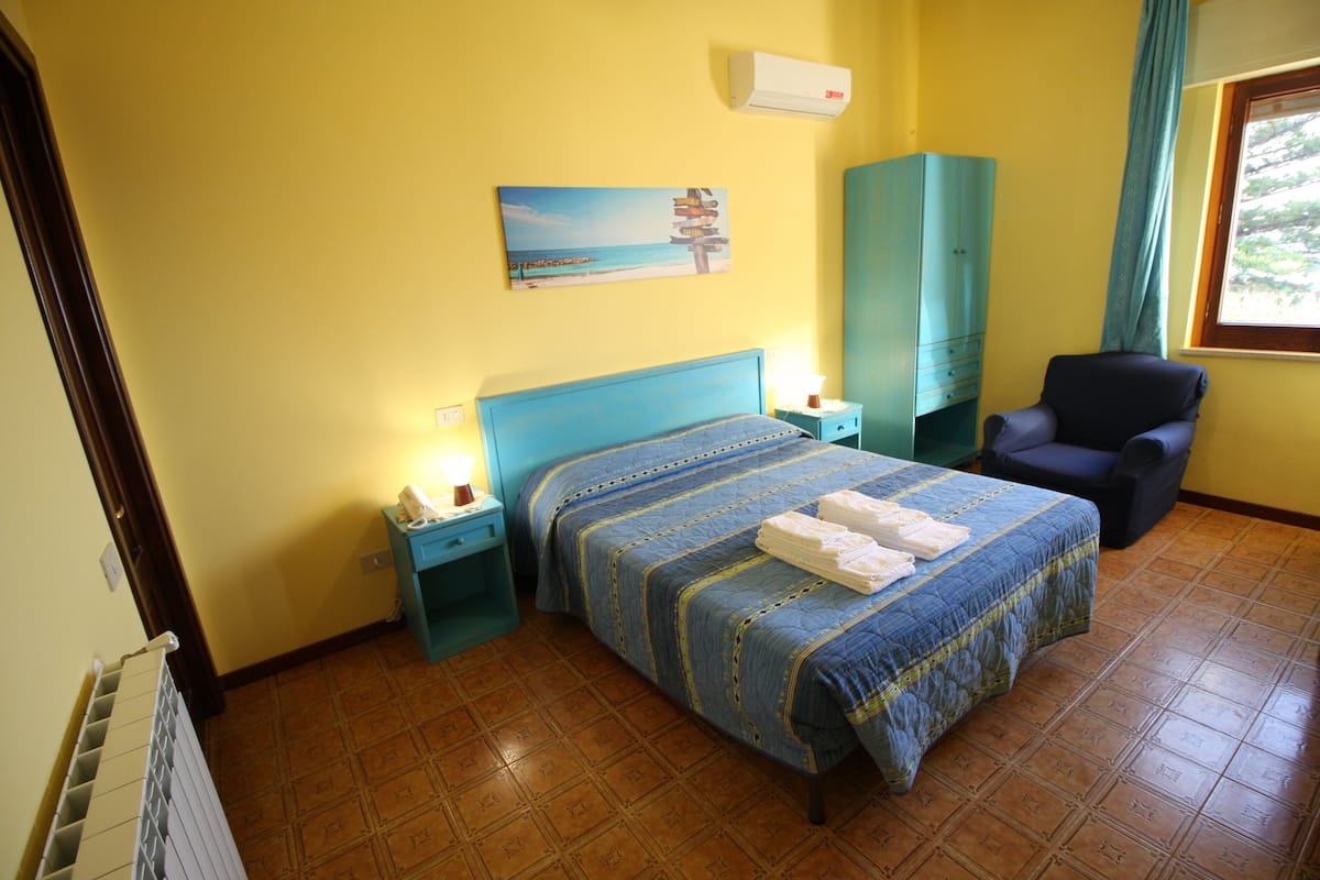 A bedroom with a bed, a nightstand, a chair, a wardrobe, and a painting on the wall.