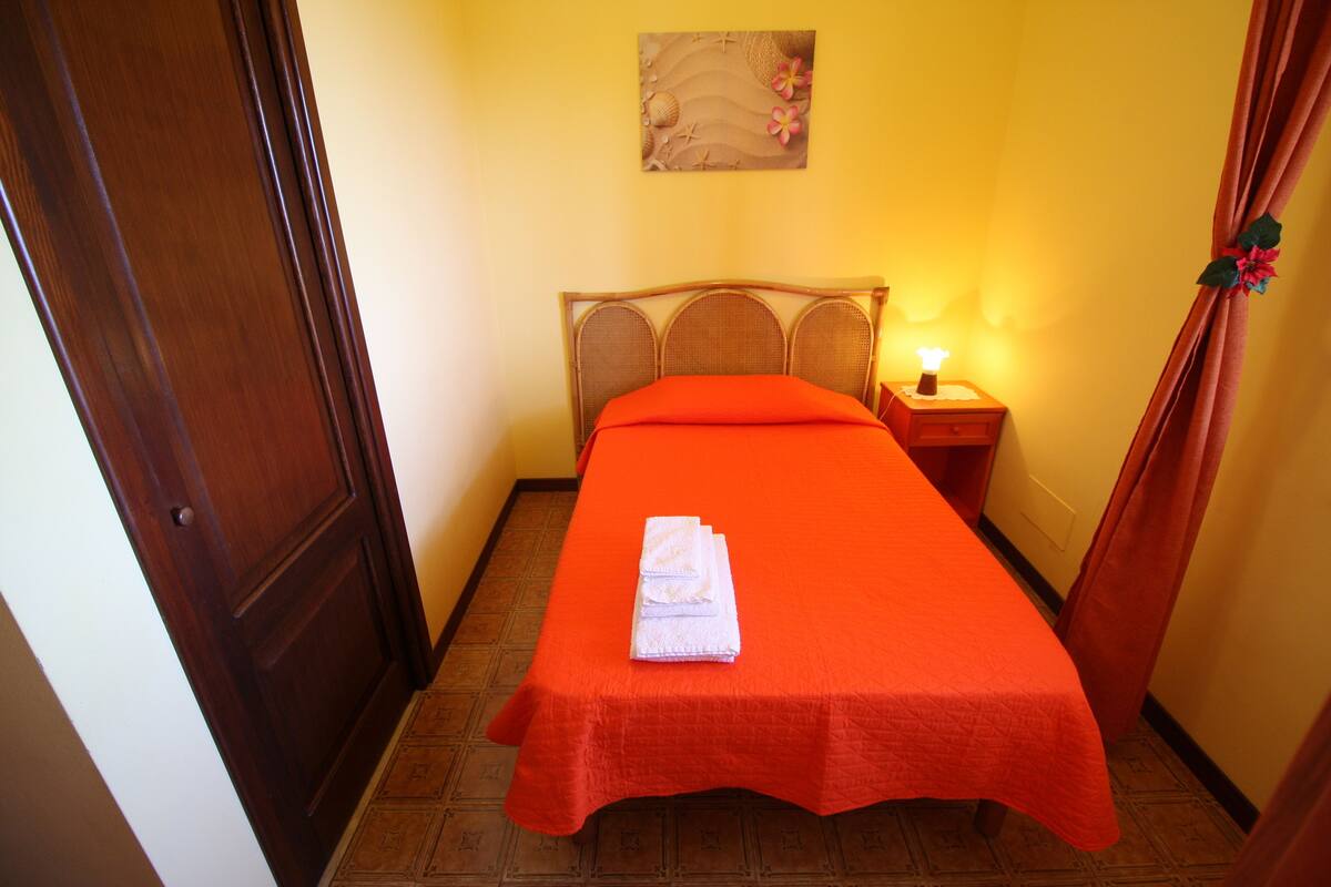 A room with a bed, a nightstand with a lamp, and a door.