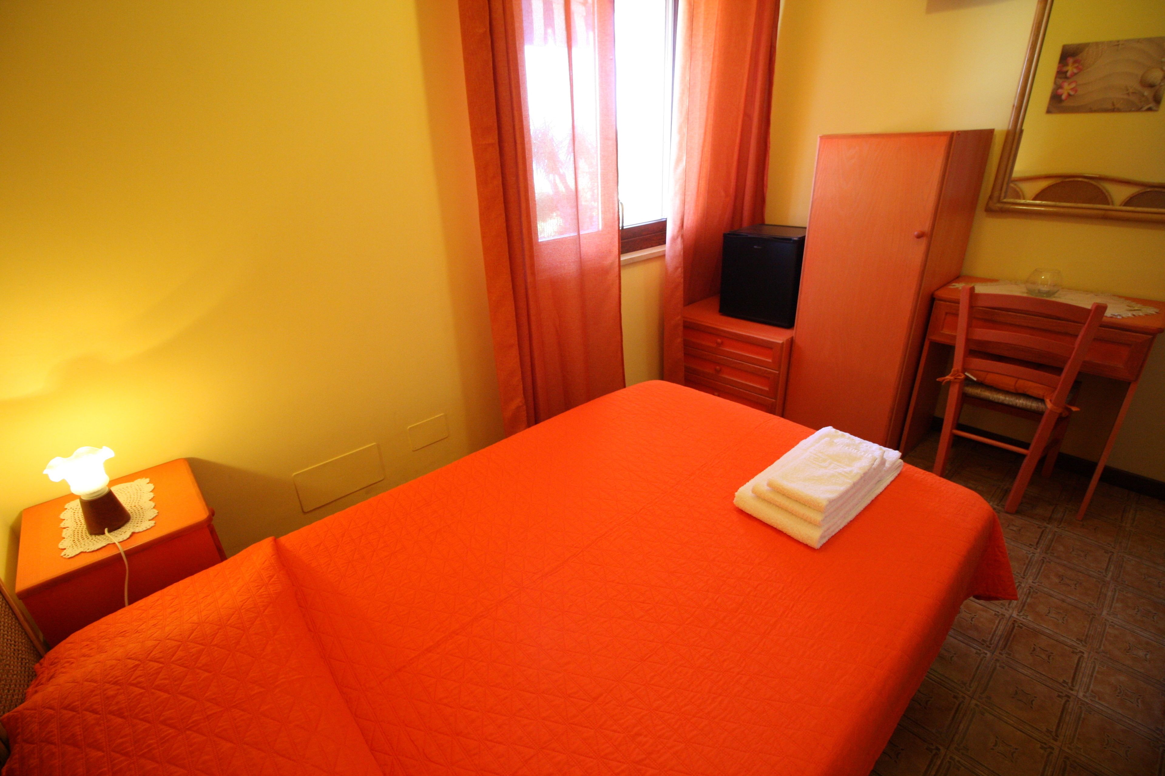 Ein Zimmer mit einem Bett, einem Schreibtisch, einem Sessel, einem Fernseher und einem Nachttisch mit einer Lampe.