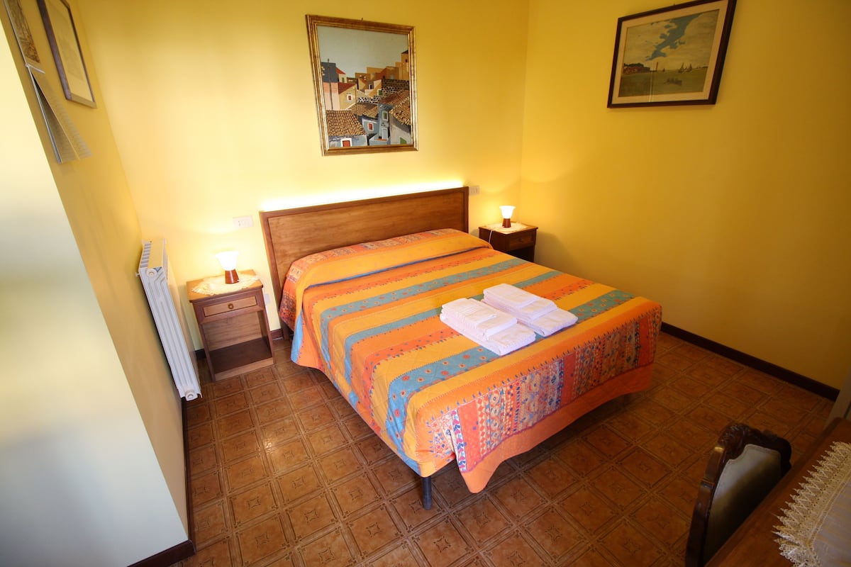 A bedroom with a wooden headboard, a bed with a striped bedspread, two bedside tables with lamps, and a radiator.